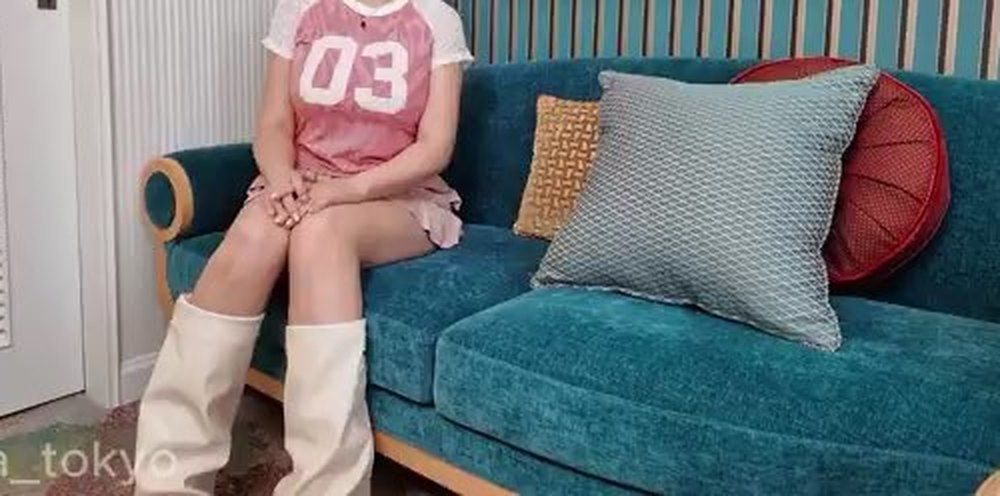 ソファに座る女性の首から下。「03」のロゴ入りピンクのTシャツに白いロングブーツ